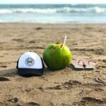 trucker hat on beach with coconut and flip flops