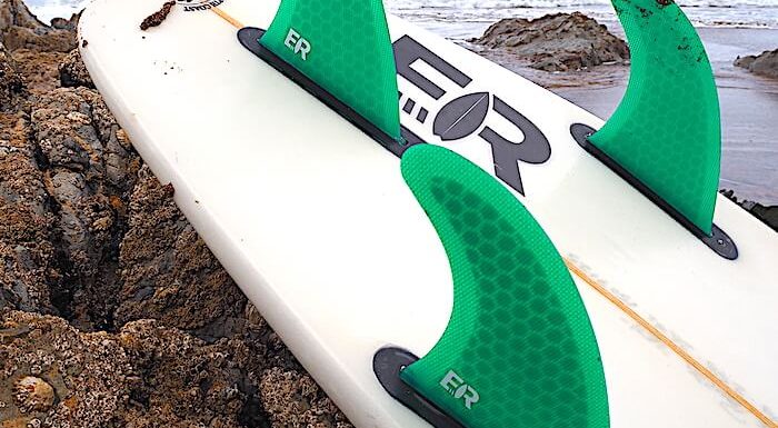 surfboard with green fins leaning against rocks on beach